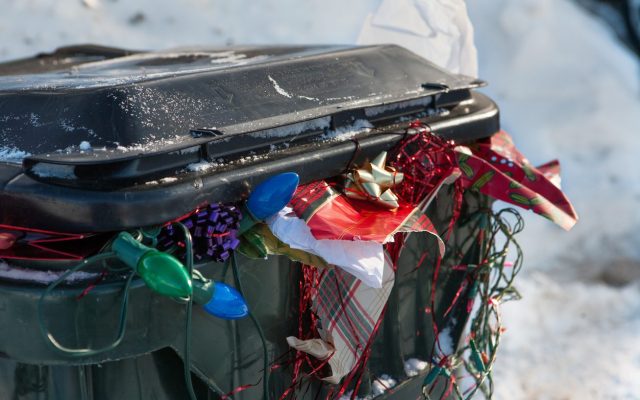 a large plastic trashbin overflowing with garbage and discarded Christmas paper lights bows etc