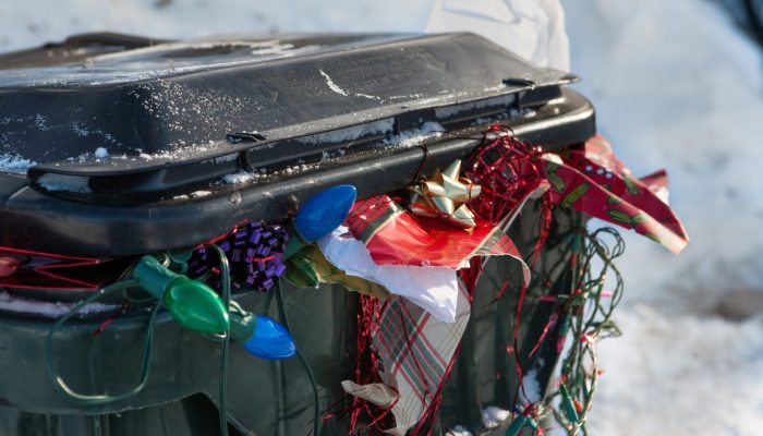 a large plastic trashbin overflowing with garbage and discarded Christmas paper lights bows etc